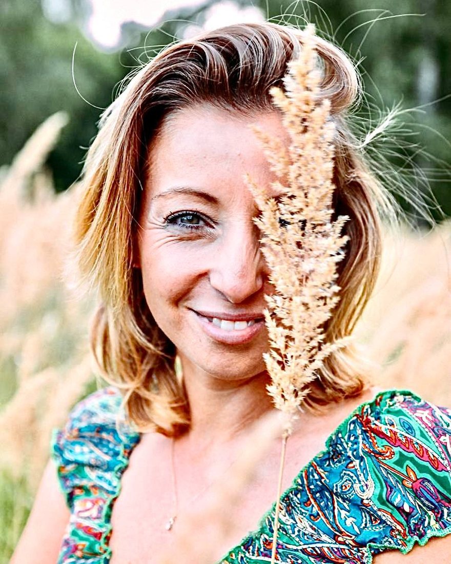 Anja Staufenbiel lächelnd im Gras, ein Grashalm vor dem Gesicht